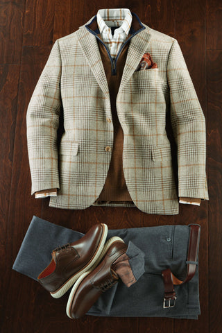Plaid blazer, brown shoes, and gray pants arranged on a wooden surface