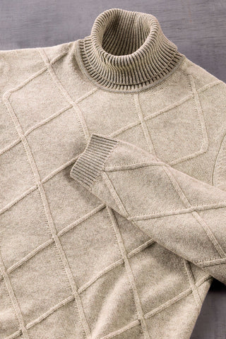 A close-up of a beige knit turtleneck sweater with a diamond grid pattern, laid flat on a dark gray textured surface.