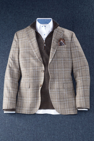 A men's tweed blazer in a brown and beige plaid pattern, styled over a brown zip-up sweater vest, white collared shirt, and a patterned pocket square, displayed on a textured blue background.