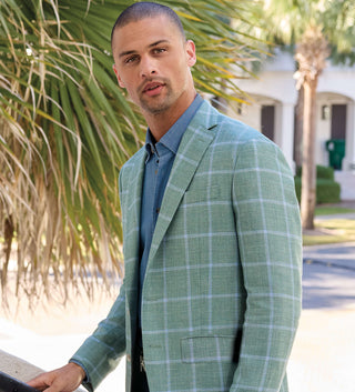 Man wearing a green checkered blazer outdoors with palm trees in the background