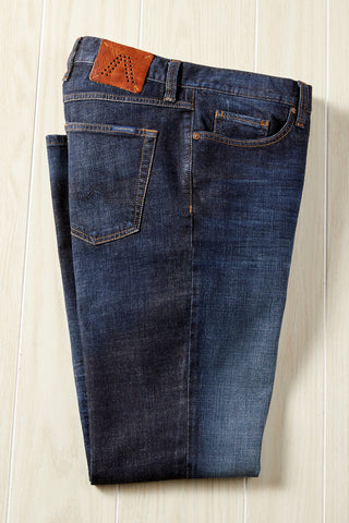 Pair of blue jeans with a brown patch on a light wooden surface